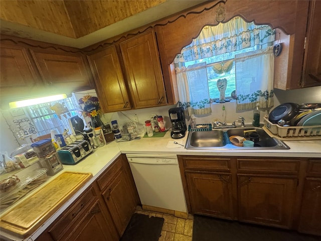 kitchen with brown cabinetry, a sink, light countertops, and white dishwasher