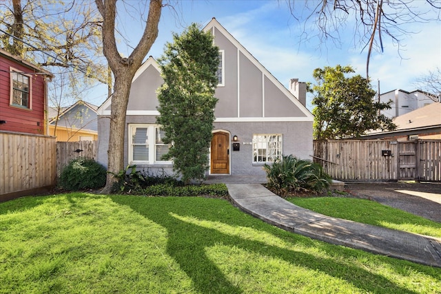 tudor home with stucco siding, a front lawn, fence, brick siding, and a chimney