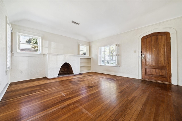 unfurnished living room featuring vaulted ceiling, visible vents, a fireplace with raised hearth, and hardwood / wood-style flooring