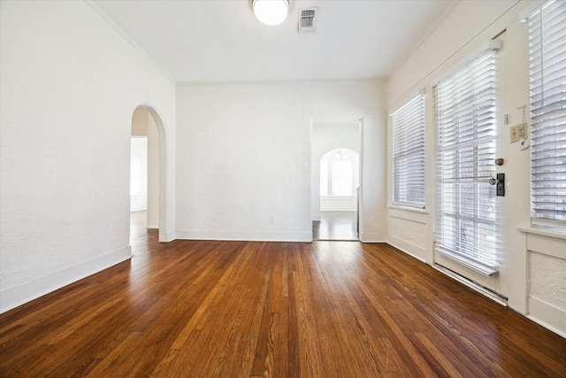 empty room with wood finished floors, visible vents, arched walkways, and baseboards