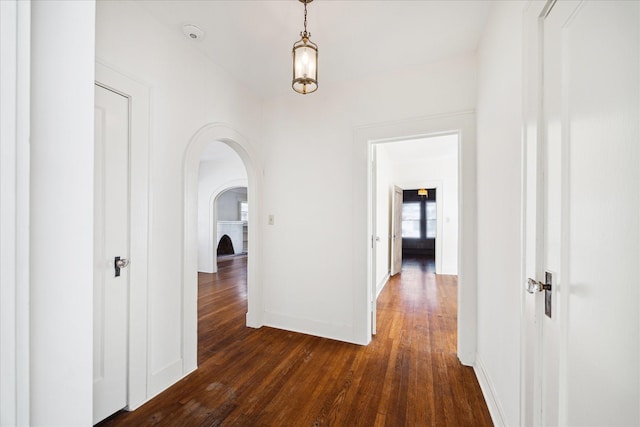 corridor with baseboards, arched walkways, and dark wood finished floors