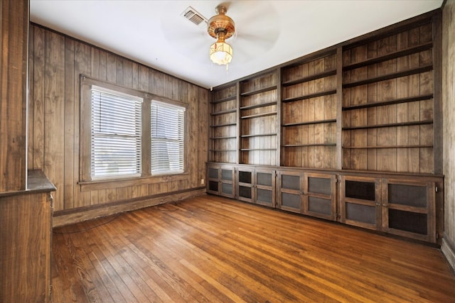 spare room with wooden walls, visible vents, a ceiling fan, and wood-type flooring