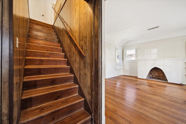 staircase featuring visible vents, wood finished floors, a fireplace, and vaulted ceiling