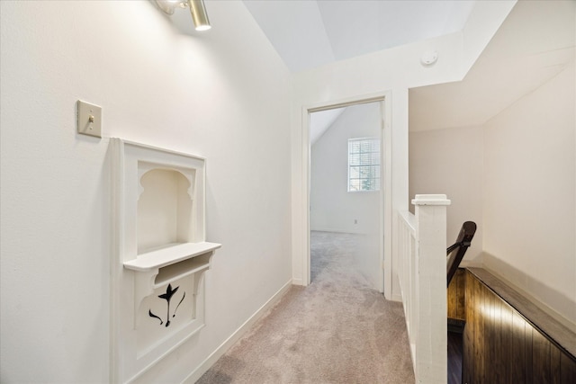 hallway featuring vaulted ceiling, an upstairs landing, baseboards, and light carpet