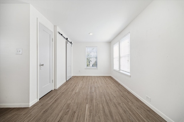 unfurnished bedroom with a barn door, wood finished floors, and baseboards