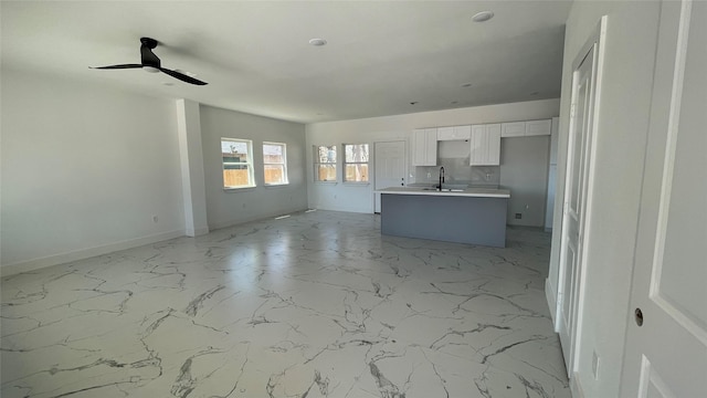 unfurnished living room with marble finish floor, baseboards, ceiling fan, and a sink