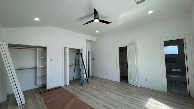 unfurnished bedroom with visible vents, baseboards, multiple closets, vaulted ceiling, and wood finished floors