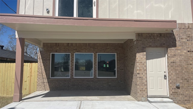 doorway to property featuring brick siding, board and batten siding, and fence