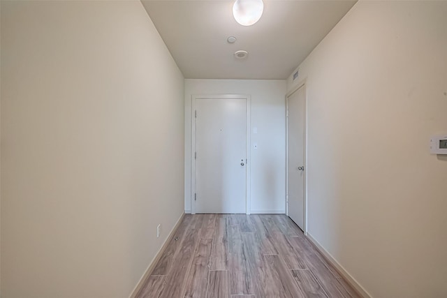 hall featuring visible vents, light wood-style flooring, and baseboards