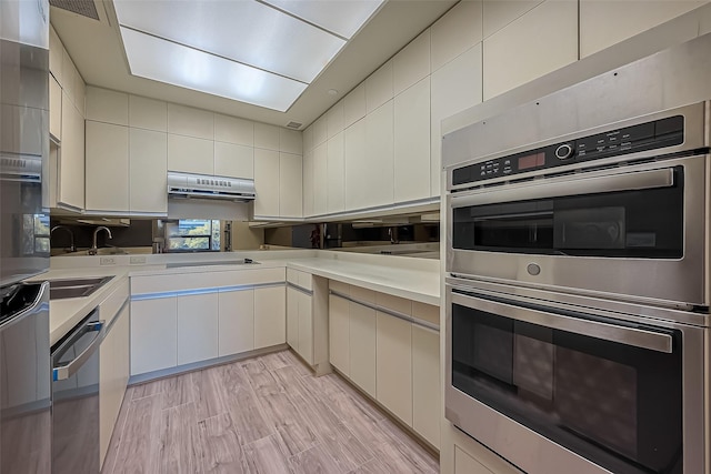 kitchen with appliances with stainless steel finishes, light wood-style flooring, white cabinets, and light countertops