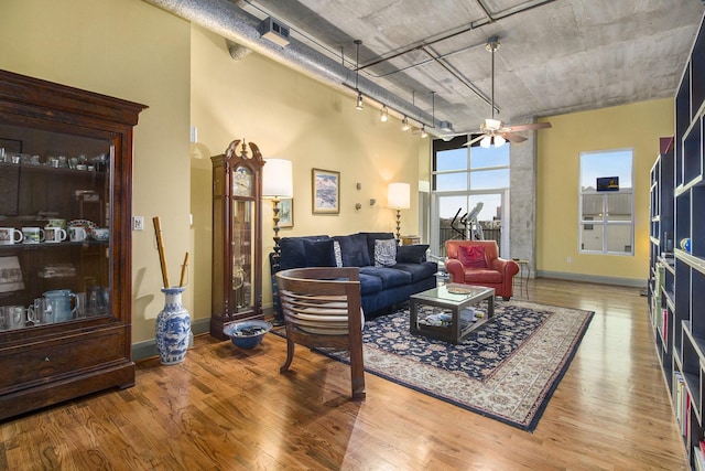 living area with baseboards, a high ceiling, a ceiling fan, and wood finished floors