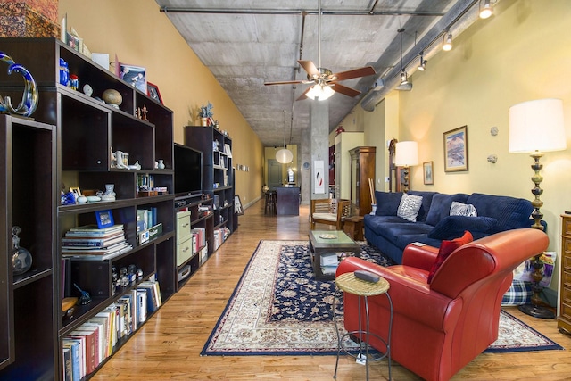 living area with rail lighting, a towering ceiling, wood finished floors, and a ceiling fan