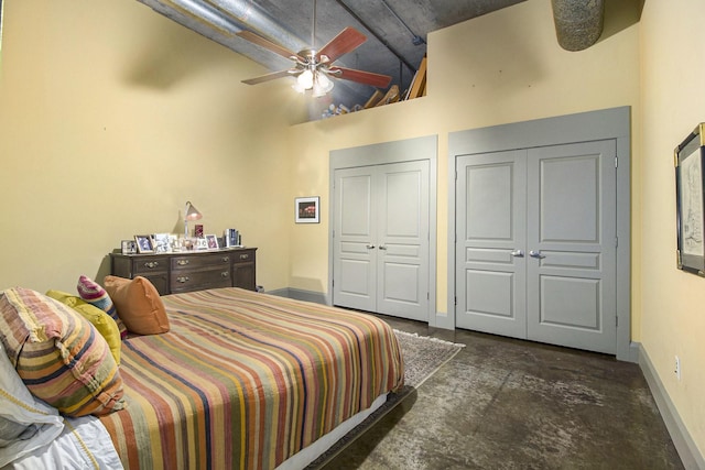 bedroom with baseboards, concrete flooring, a towering ceiling, and multiple closets