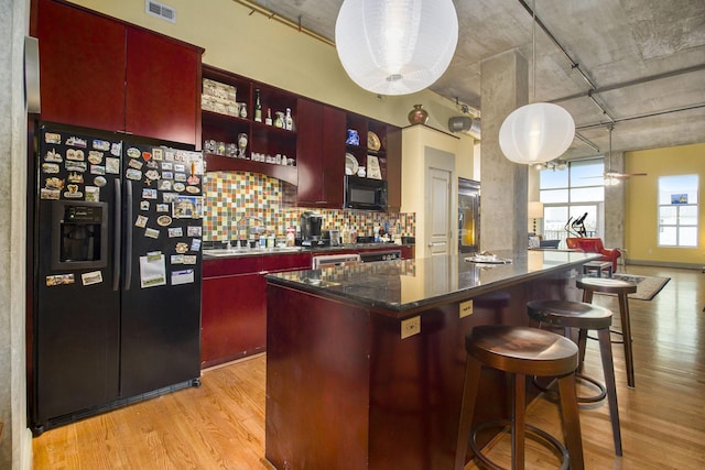 kitchen with dark countertops, visible vents, light wood-style flooring, black appliances, and a sink