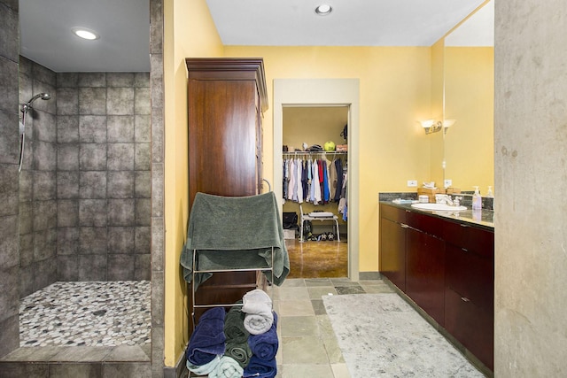 bathroom featuring vanity, tiled shower, recessed lighting, stone tile flooring, and a spacious closet