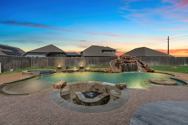 pool at dusk with a fenced backyard, a pool with connected hot tub, and a fire pit