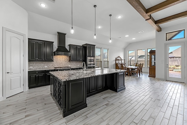 kitchen featuring tasteful backsplash, light wood finished floors, premium range hood, appliances with stainless steel finishes, and dark cabinetry