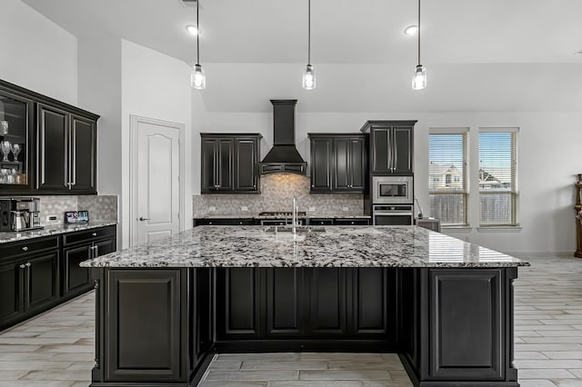 kitchen with an island with sink, a sink, stainless steel appliances, custom exhaust hood, and hanging light fixtures