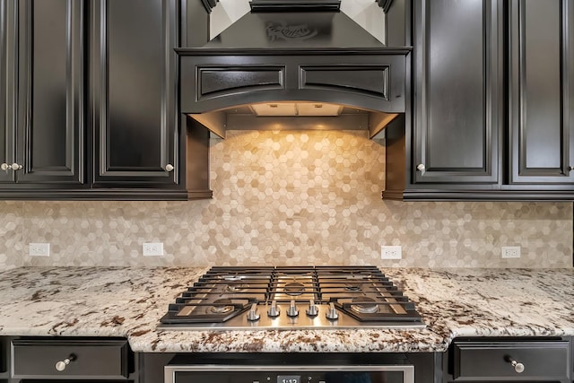 kitchen with dark cabinetry, premium range hood, backsplash, and stainless steel gas cooktop