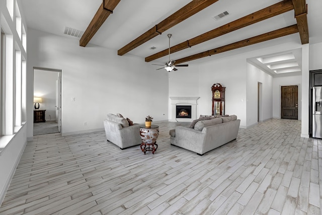 living room featuring a lit fireplace, visible vents, light wood-style floors, and ceiling fan