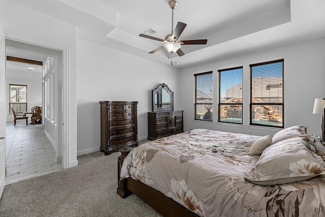 bedroom featuring visible vents, carpet flooring, a tray ceiling, and multiple windows