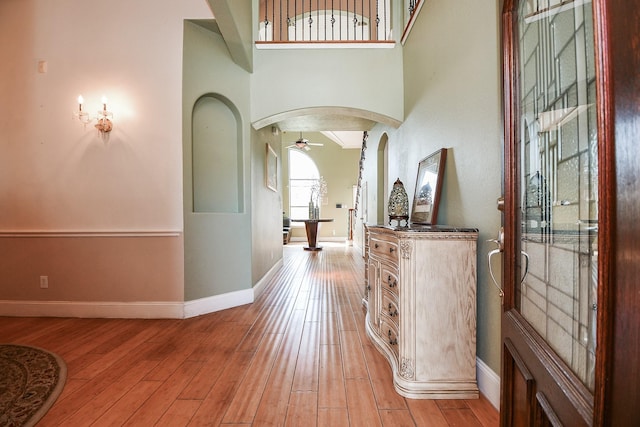 corridor with light wood-style floors, arched walkways, a towering ceiling, and baseboards