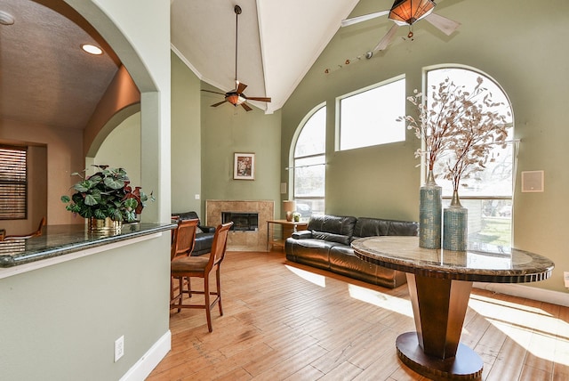 living room with wood finished floors, high vaulted ceiling, arched walkways, ceiling fan, and a glass covered fireplace