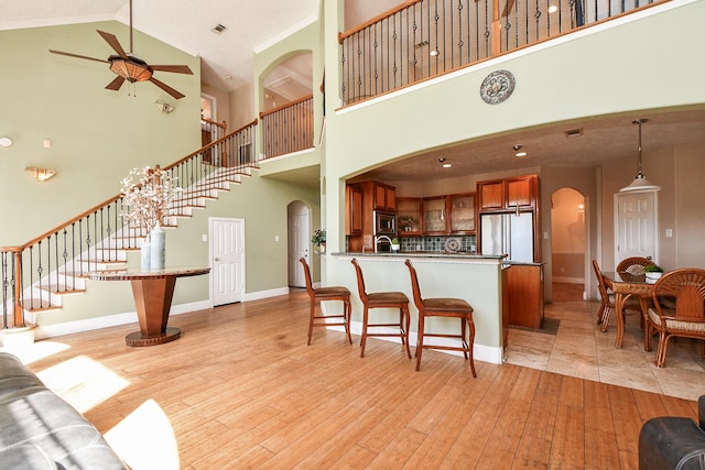 living room with baseboards, arched walkways, ceiling fan, stairs, and light wood-style floors