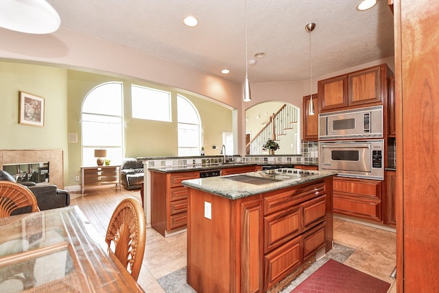 kitchen with arched walkways, stovetop with downdraft, wall oven, stainless steel microwave, and open floor plan