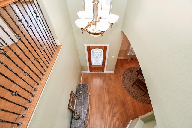 foyer with baseboards, a towering ceiling, arched walkways, a notable chandelier, and wood-type flooring