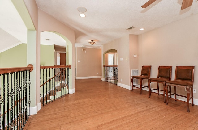 living area featuring light wood-type flooring, visible vents, arched walkways, baseboards, and ceiling fan