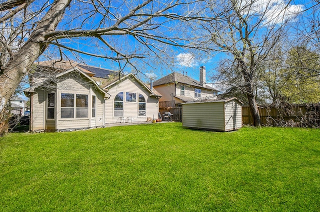 back of property featuring a fenced backyard, a yard, a storage shed, an outdoor structure, and solar panels