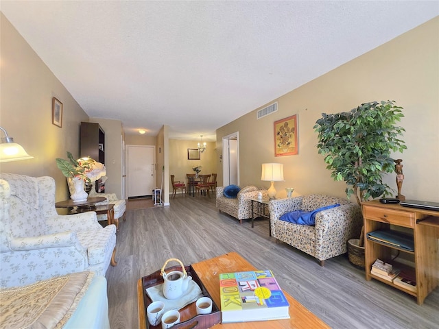 living room featuring an inviting chandelier, wood finished floors, visible vents, and a textured ceiling