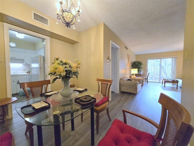 dining room with visible vents, a textured ceiling, an inviting chandelier, and wood finished floors