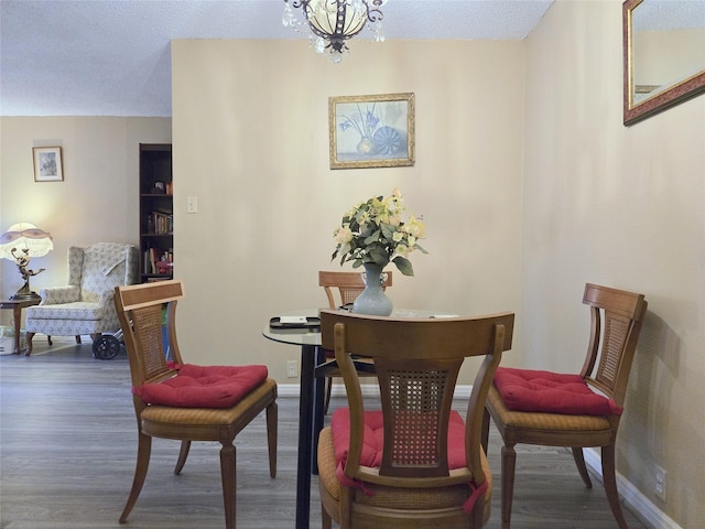 dining space featuring a chandelier, a textured ceiling, baseboards, and wood finished floors