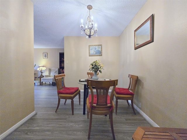 dining room with a chandelier, a textured ceiling, baseboards, and wood finished floors