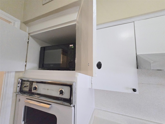 interior details featuring oven, white cabinets, and black microwave