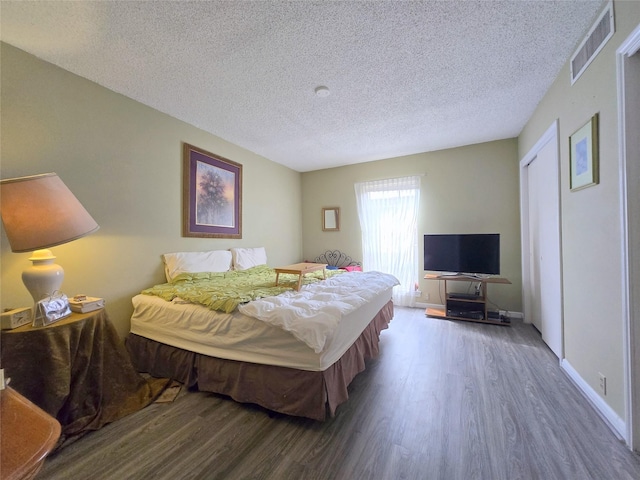 bedroom with visible vents, a textured ceiling, baseboards, and wood finished floors