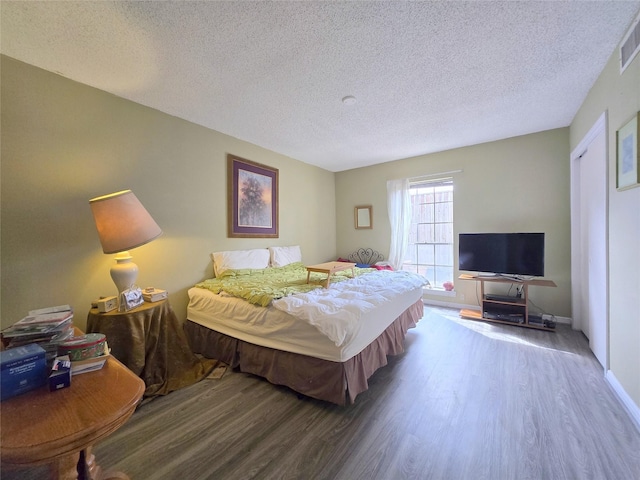 bedroom with baseboards, wood finished floors, visible vents, and a textured ceiling