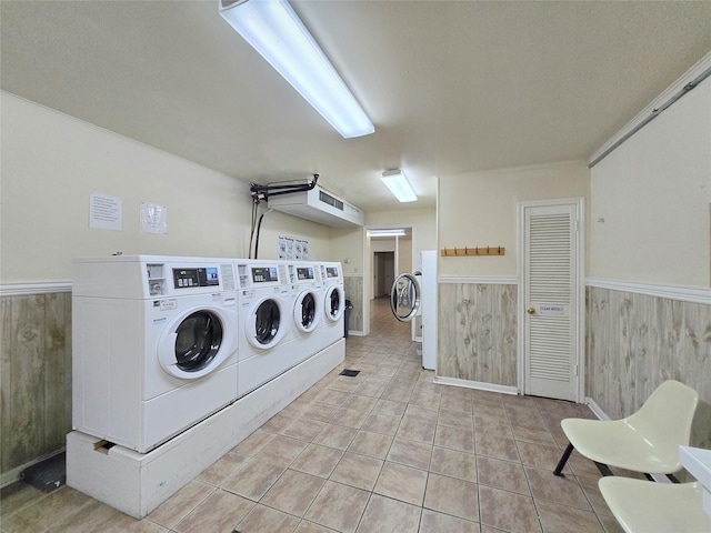 common laundry area with light tile patterned flooring, a wainscoted wall, wood walls, and separate washer and dryer