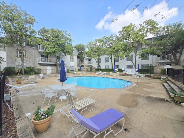 community pool with a patio area, fence, and a residential view