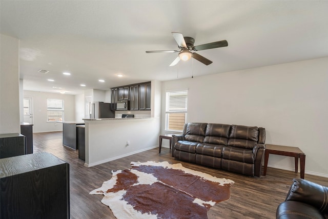 living room featuring dark wood finished floors, a ceiling fan, baseboards, and a healthy amount of sunlight