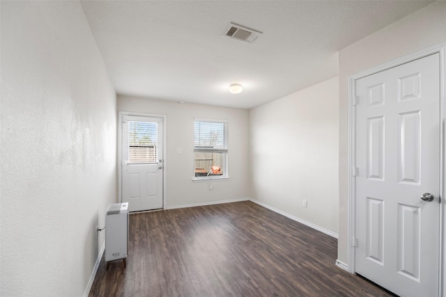 empty room featuring dark wood finished floors, visible vents, heating unit, and baseboards