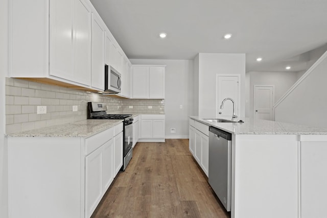 kitchen featuring backsplash, a center island with sink, light wood-style flooring, appliances with stainless steel finishes, and a sink