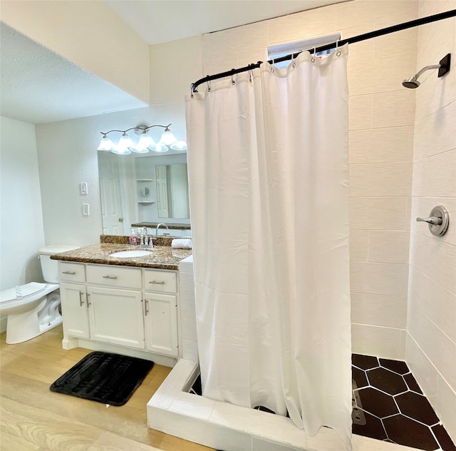 bathroom featuring wood finished floors, toilet, a stall shower, and vanity