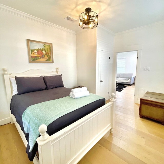 bedroom with light wood finished floors, visible vents, and ornamental molding