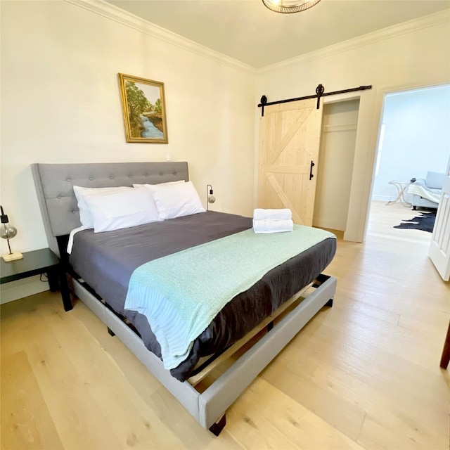 bedroom with a barn door, light wood-type flooring, and ornamental molding