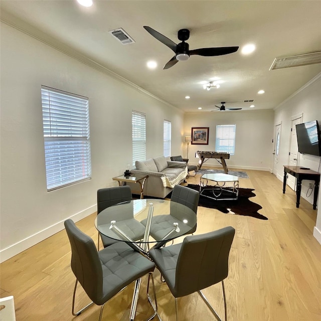 dining room featuring visible vents, ornamental molding, a ceiling fan, light wood-style floors, and baseboards