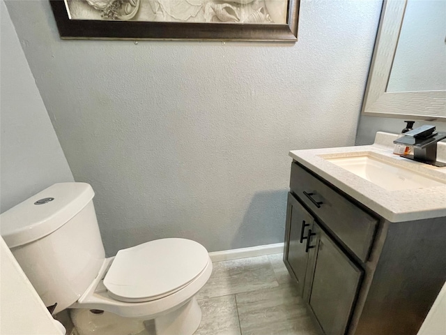 bathroom featuring toilet, vanity, and a textured wall