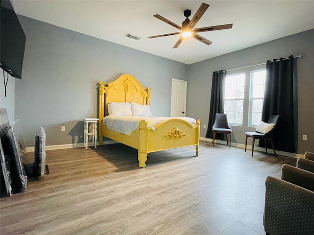 bedroom featuring ceiling fan, visible vents, baseboards, and wood finished floors